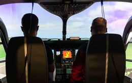 2 Personen sitzen im Cockpit des Flugsimulators und blicken auf eine Landschaft.