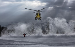 Ein Christophorus-Hubschrauber wird in einer Schneelandschaft von einer Person zur Landung eingewiesen. Der Einweiser hält beide Arme nach oben