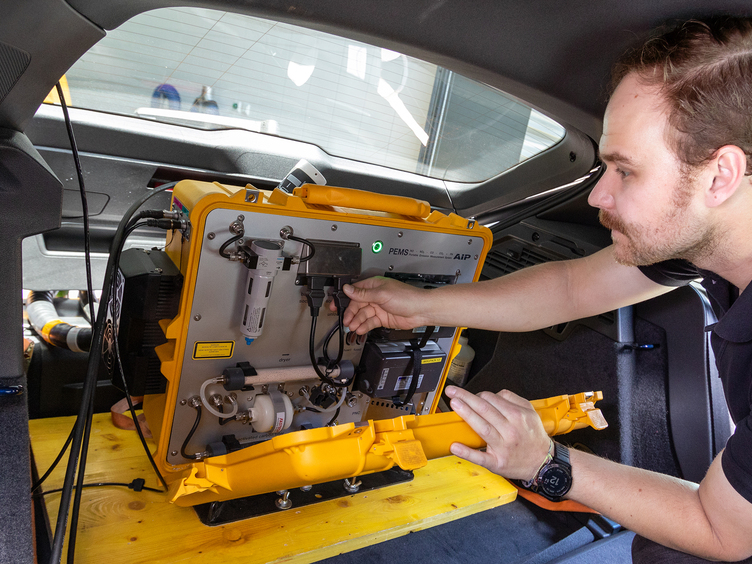 Ein Techniker arbeitet an einem mobilen Abgasmessgerät im Kofferraum eines Autos.