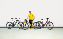auto touring-Redakteur mit 3 E-Bikes unter 20 kg vor weißer Wand. Das Wallis Project S, das MyEsel E-Gravel und das Kraftstoff E-Razzo Wave.