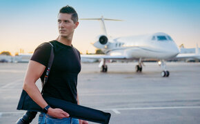 Fotograf Daniel Gossmann steht mit Kamera auf einem Flughafen, im Hintergrund ein Jet.