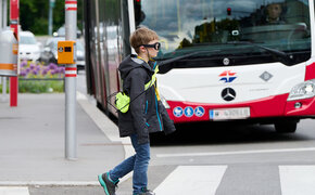 Ein Kind mit einer Blickbewegungsbrille überquert die Straße. Im Hintergrund sieht man einen Autobus.