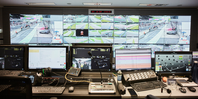 Der Race-Controll-Room des Red Bull Rings mit einer Wand voller Bildschirme, im Vordergrund befinden sich viele Laptops und Tastaturen. 