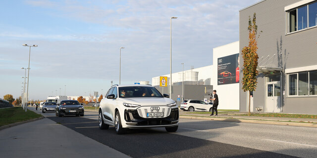 Ein weißer Audi fährt an einem grauen Gebäude vorbei