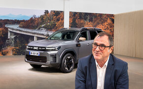 Dacia-CEO Denis Le Vot. Im Hintergrund steht ein graues SUV in einem Studio.