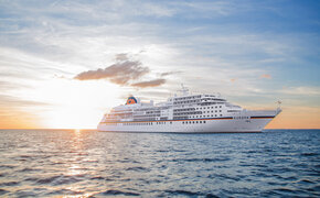 Zu sehen ist die MS Europa in Seitenansicht bei Sonnenuntergang auf hoher See.