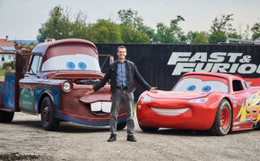 Martin Hahn steht vor den Filmautos aus Cars, Lightning McQueen (links) und Hook (rechts)