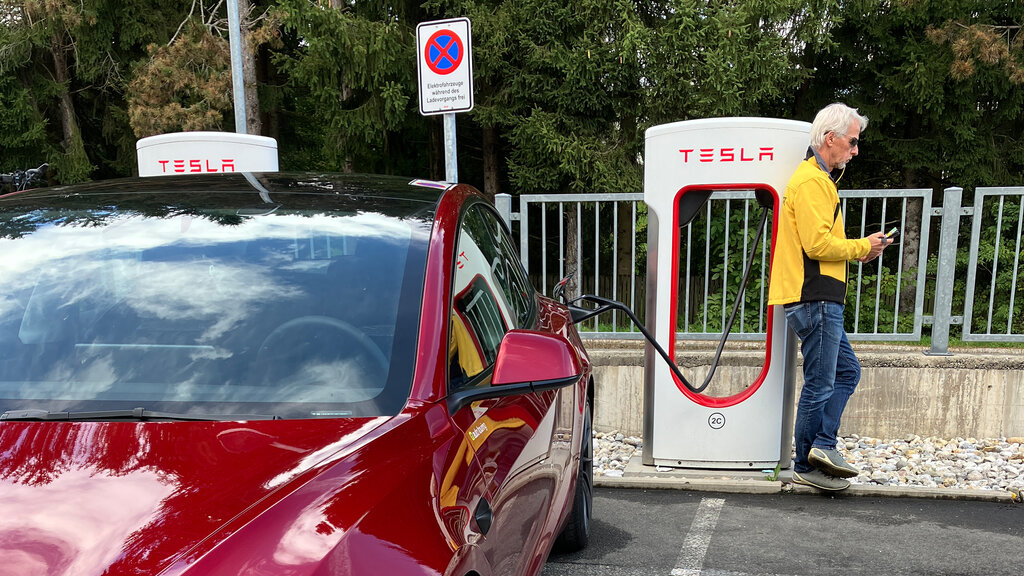 Ein rotes Auto lädt, an der Ladestation lehnt ein Mann in gelber Jacke