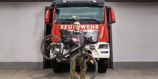 Feuerwehrmann Hannes Heiss steht vor einem Feuerwehrauto. Neben ihm sein Fahrrad.