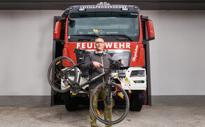 Feuerwehrmann Hannes Heiss steht vor einem Feuerwehrauto. Neben ihm sein Fahrrad.