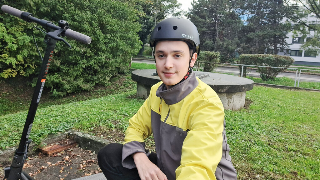 Selfie eines jungen Burschen mit Helm, der neben einem E-Scooter kniet