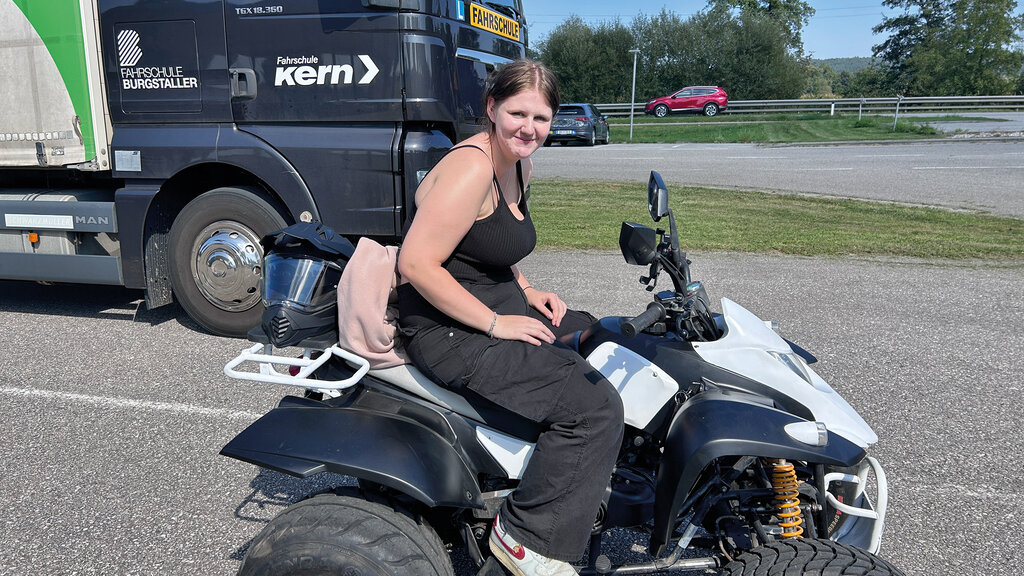 Ein Mädchen sitzt auf einem Quad, im Hintergrund ein Lkw