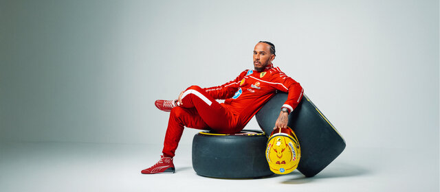 Lewis Hamilton sitzt im Ferrari-Rennanzug auf zwei Formel 1-Rädern