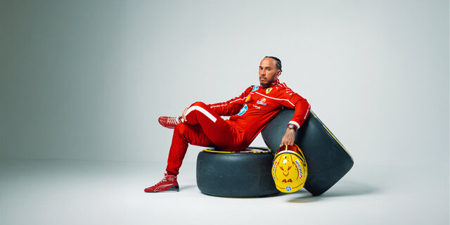 Lewis Hamilton sitzt im Ferrari-Rennanzug auf zwei Formel 1-Rädern