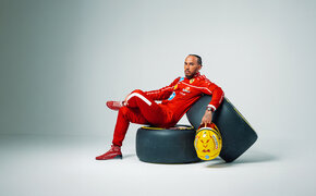 Lewis Hamilton sitzt im Ferrari-Rennanzug auf zwei Formel 1-Rädern