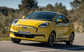 Ein gelber Ford Puma Gen-E fährt durch eine Kurve auf einer Landstraße.