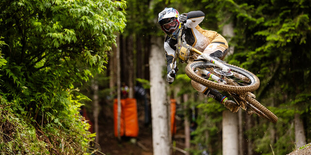 Mountainbike-Profi Vali Höll im Sprung auf einer Downhill-Strecke im Wald.