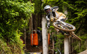 Mountainbike-Profi Vali Höll im Sprung auf einer Downhill-Strecke im Wald.