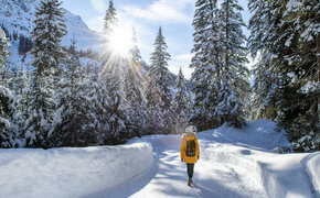 Eine Frau in einem gelben Anorak spaziert durch einen verschneiten Wald. 