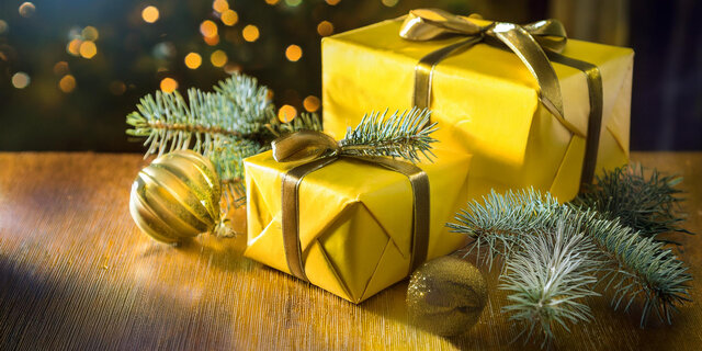 Zu sehen ist ein weihnachtliches Motiv: Geschenke mit goldenen Maschen und Tannenzweigen, die auf einem Tisch stehen. 