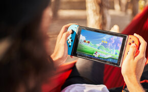 Nicht erkennbare Person mit einer Verschlusskappe, die Videospiele auf einer tragbaren Konsole spielt, während sie auf Hängematte hängt.