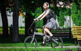 Eine junge Frau fährt mit einem Mini-Fahrrad im Park. Sie hat Kopfhörer auf.